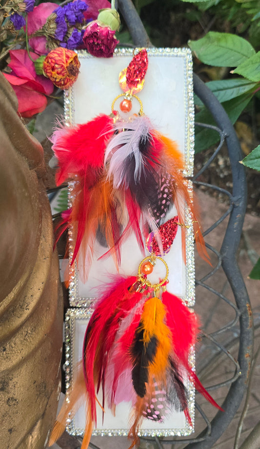 Red multicolored feather earrings by Jennivine featuring long, vibrant feathers with gold accents on hooks.